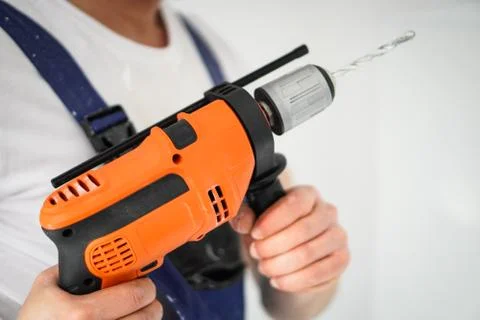 Young professional worker with drill making a hole in white wall. Stock Photos