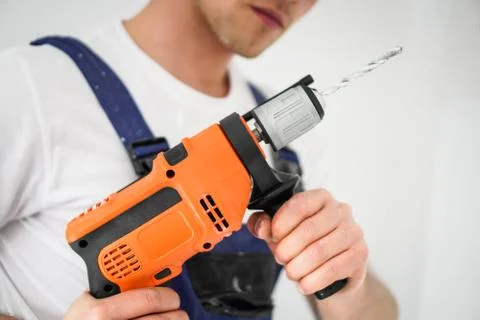 Young professional worker with drill making a hole in white wall. Stock Photos