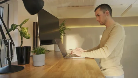 A young professional working at a laptop transitions from standing to sitting Stock Footage