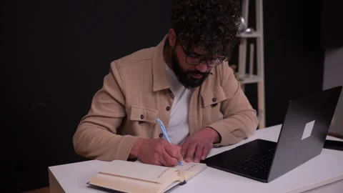 Young professional writing in a notebook while using a laptop 库存影片 346989092