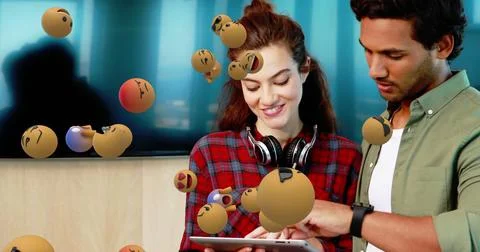 Young professionals collaborating on tablet with floating emojis in modern Stock Illustration