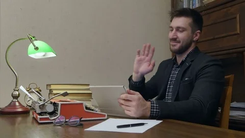 Young professor sitting at his study table and having a video call via tablet Vídeos de archivo 73690046