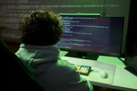 A young programmer codes intently in a dark setting, immersed in his work and Stockfoto's