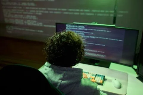 A young programmer codes intently in a dark setting, immersed in his work and 库存照片
