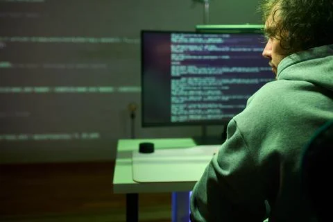 A young programmer codes intently in a dark setting, immersed in his work and Stockfoto's