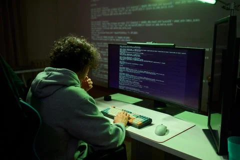 A young programmer codes intently in a dark setting, immersed in his work and Stockfoto's