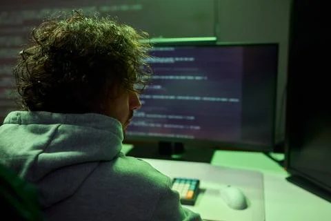 A young programmer codes intently in a dark setting, immersed in his work and Stockfoto's
