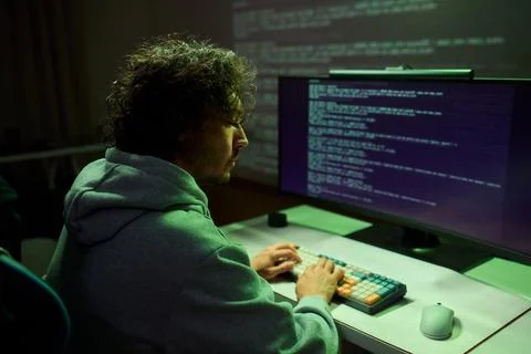 A young programmer codes intently in a dark setting, immersed in his work and Foto stock