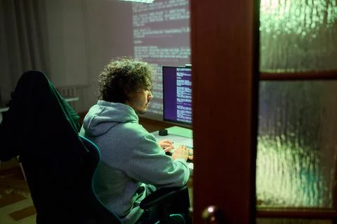 A young programmer codes intently in a dark setting, immersed in his work and Stock Photos