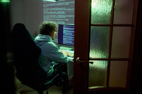 A young programmer codes intently in a dark setting, immersed in his work and Stock Photos