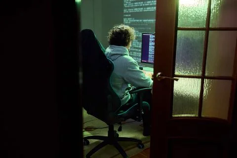 A young programmer codes intently in a dark setting, immersed in his work and 库存照片