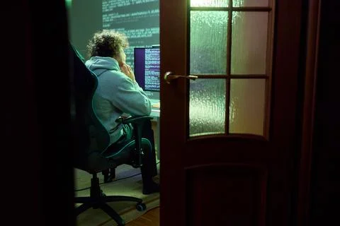 A young programmer codes intently in a dark setting, immersed in his work and Stockfoto's