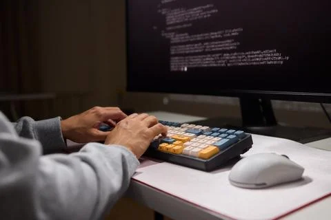 A young programmer codes intently in a dark setting, immersed in his work and Stock Photos