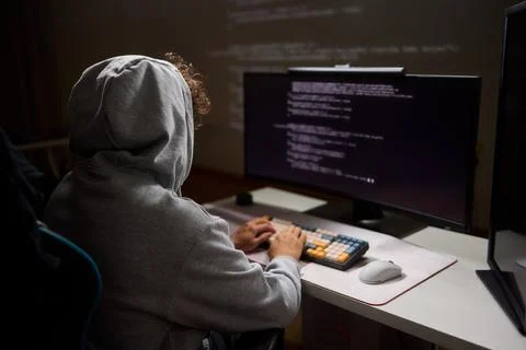 A young programmer codes intently in a dark setting, immersed in his work and Stockfoto's