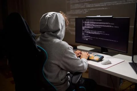 A young programmer codes intently in a dark setting, immersed in his work and Stock Photos