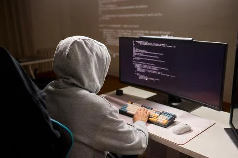 A young programmer codes intently in a dark setting, immersed in his work and Stockfoto's