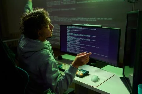 A young programmer codes intently in a dark setting, immersed in his work and Stockfoto's