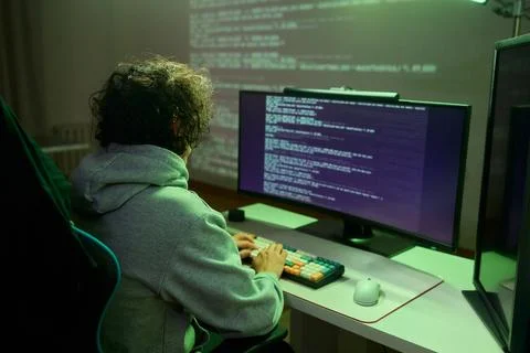 A young programmer codes intently in a dark setting, immersed in his work and 库存照片