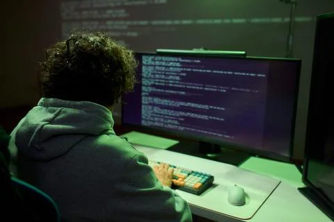 A young programmer codes intently in a dark setting, immersed in his work and Stockfoto's
