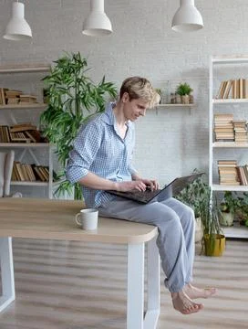 A young programmer guy is sitting on top of a table with his legs hanging dow Stock Photos