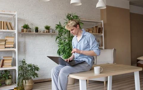 A young programmer guy is sitting on top of a table with his legs hanging dow Stock Photos