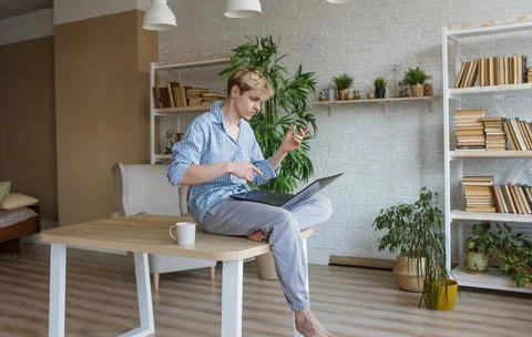 A young programmer guy is sitting on top of a table with his legs hanging dow Stock Photos