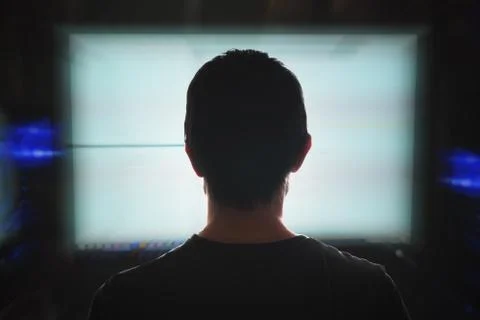 Young programmer is looking at computer screen at night. View from behind. Stock-Fotos