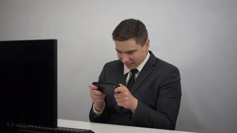 A young programmer plays a game on the phone. Businessman plays at work in the Stock Footage 231001509