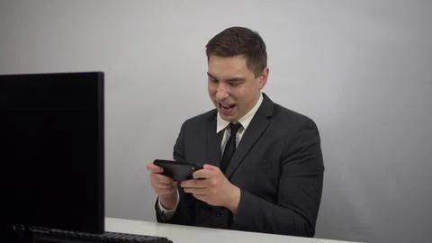 A young programmer plays a game on the phone. Businessman plays at work in the Stock Photos