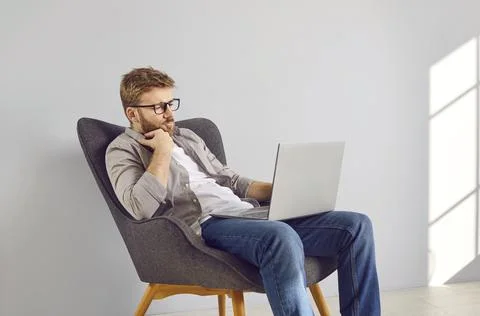 Young programmer is sitting in armchair, working on laptop computer, and 写真素材