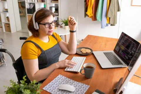 Young programmer sitting by desk at home, eating cookies with tea and working Foto stock