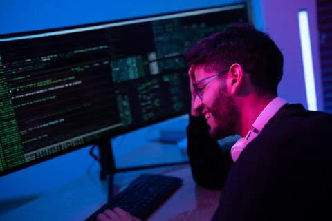 Young programmer smiles while coding in a modern workspace with vibrant blu.. Stock-Fotos