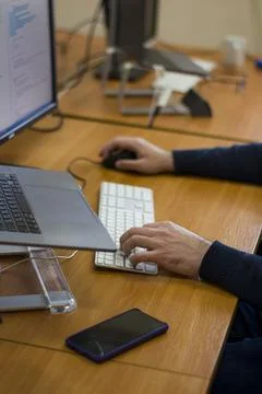 Young programmer typing on a freestanding white keyboard on a wooden table in Stock Photos