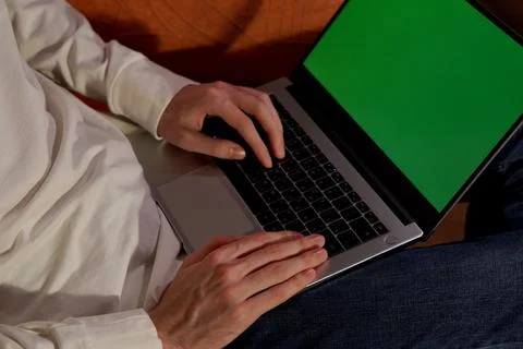 A young programmer in a white hoodie is working on a laptop with a green screen Fotos de archivo