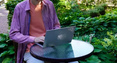 A young programmer is working on a laptop sitting at a glass table in an outdoor 写真素材