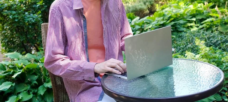 A young programmer is working on a laptop sitting at a glass table in a par.. Fotos de archivo