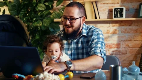 Young programmer works at a computer and holds newborns in his lap Stock Footage 156794730
