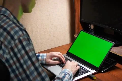 A young programmer works with his hands on a laptop with a green screen in .. 스톡 사진