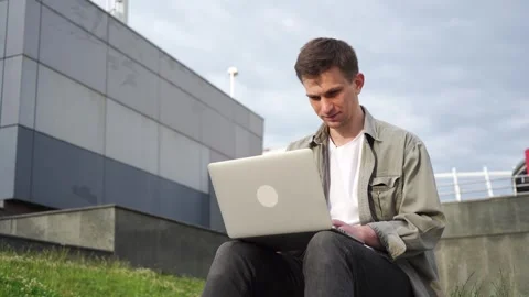 A young programmer works at his laptop outside the office. Cityscape. Stock Footage 246304534