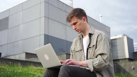 A young programmer works at his laptop outside the office. Cityscape. Stock Footage 246304605