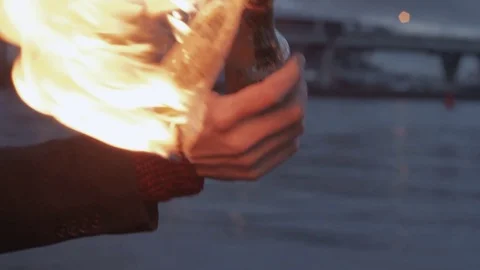 Young protester with a burning Molotov cocktail in hand standing on coast Stock Footage