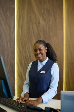 Young receptionist entering personal data of guests into database by counter Foto stock