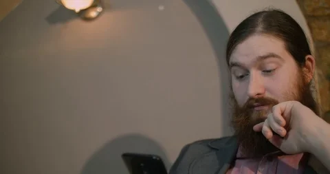 A young red-bearded man gets bad news on a smartphone Stock Footage 87323621