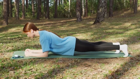 A young red-haired girl is doing outdoor sports in the forest. plank pose. Stock Footage 273538749
