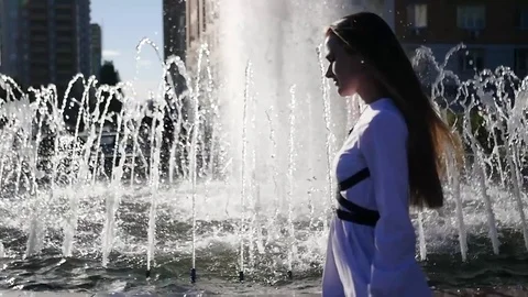 Young red-haired girl model paces in a white blouse near a refreshing fountain Stock Footage 76340531