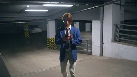 Young red-haired guy looking for someone in the parking lot.calls on the phone Vidéo 165052412