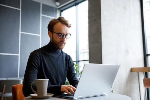 A young red-haired guy, a programmer or entrepreneur in glasses, works in a Stock Photos