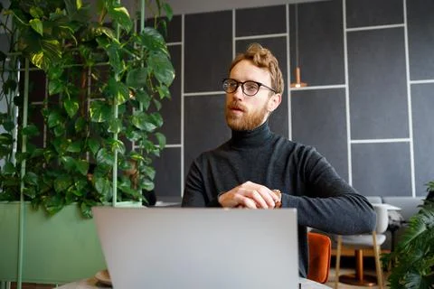 A young red-haired guy, a programmer or entrepreneur in glasses, works in a Stock Photos