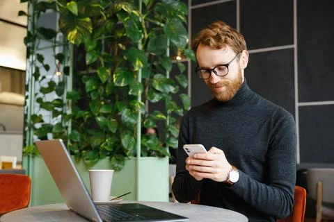 A young red-haired guy, a programmer or businessman in glasses, sits in a Stock Photos