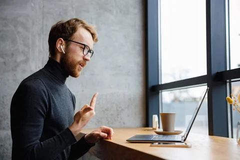 A young red-haired guy, a programmer or businessman in glasses, is sitting in a Foto stock